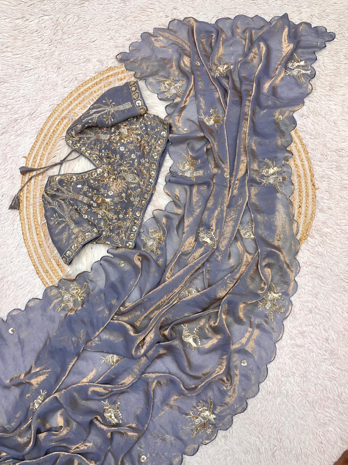 A designer grey space silk saree featuring golden embroidered bird motifs and shimmering scalloped borders. The matching stitched blouse, richly decorated with sequin and bead detailing, adds a luxurious touch to this elegant ensemble.