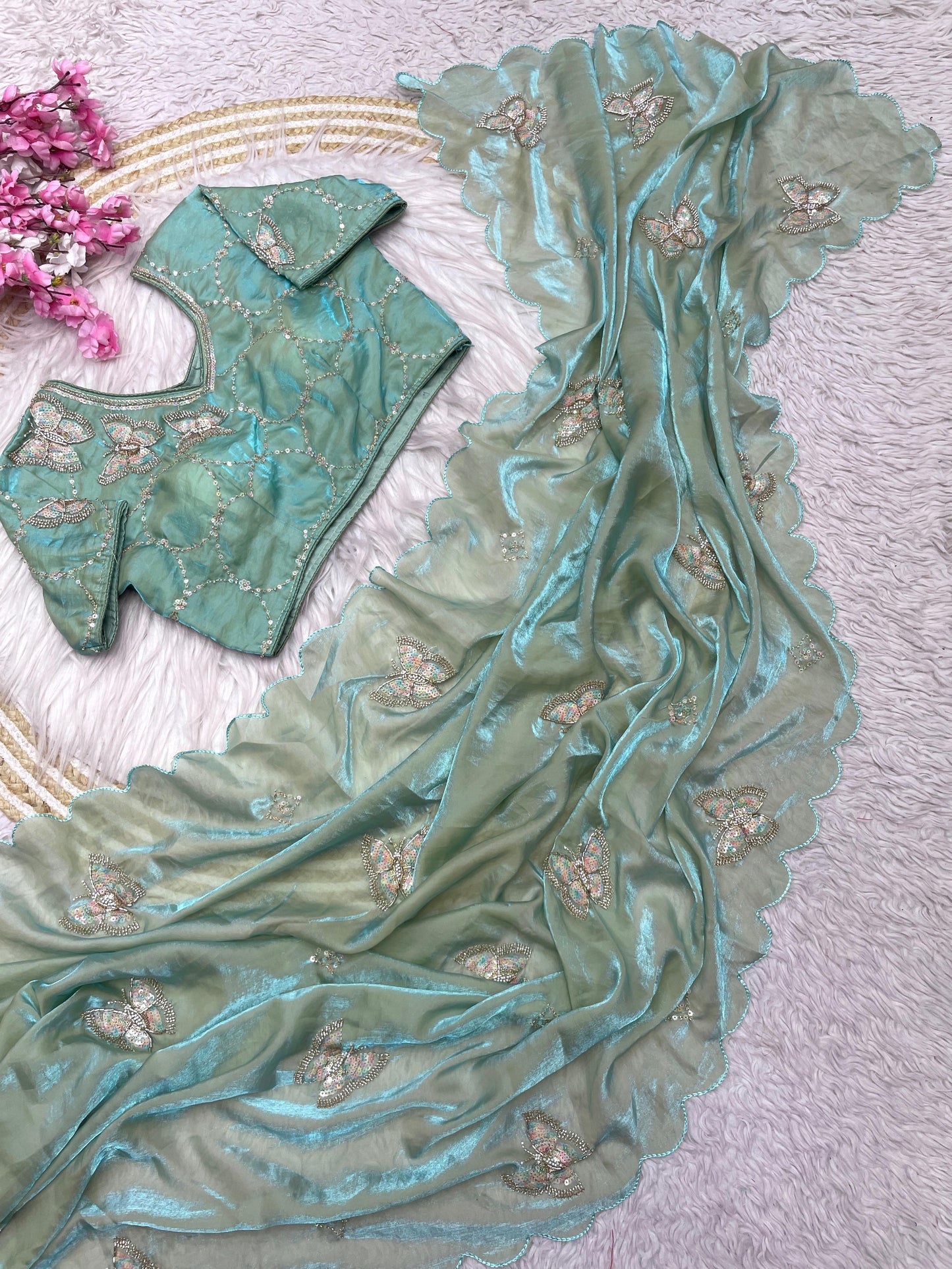 A light pista space silk saree embellished with zari and stone butterfly motifs. The scalloped border and matching stitched blouse enhance its luxurious and festive appearance.