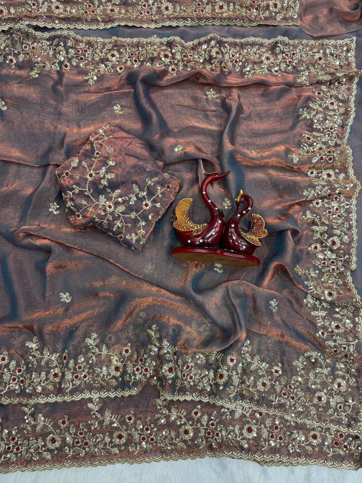 A metallic lavender Fandy silk saree beautifully detailed with golden thread embroidery and shimmering floral motifs. The scalloped border and matching blouse piece make it a stunning choice for festive and bridal wear.