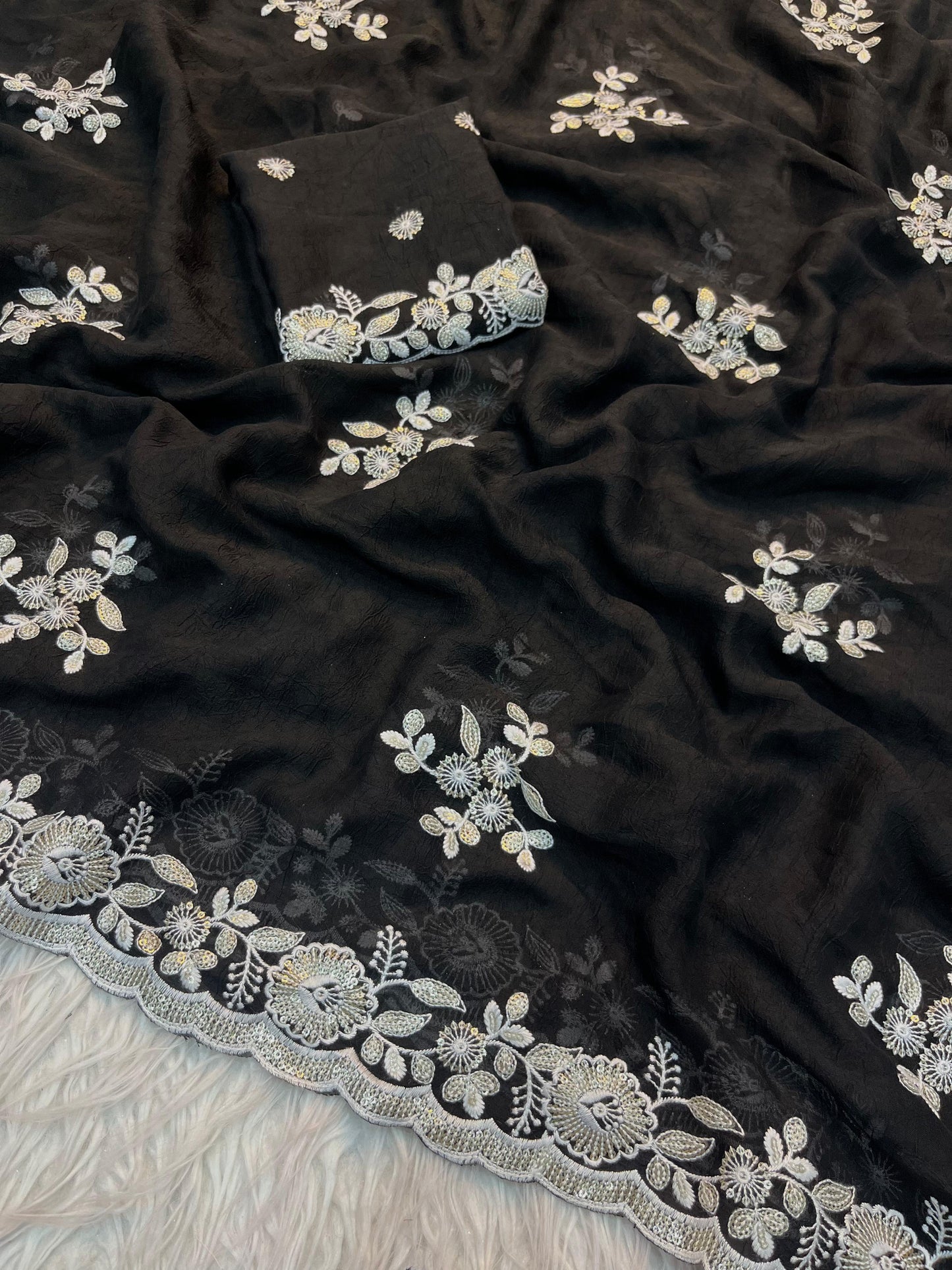 A midnight black saree beautifully embellished with silver floral lace embroidery and delicate sequin highlights. The ensemble includes a matching blouse piece, exuding charm and grace for party and festive looks.