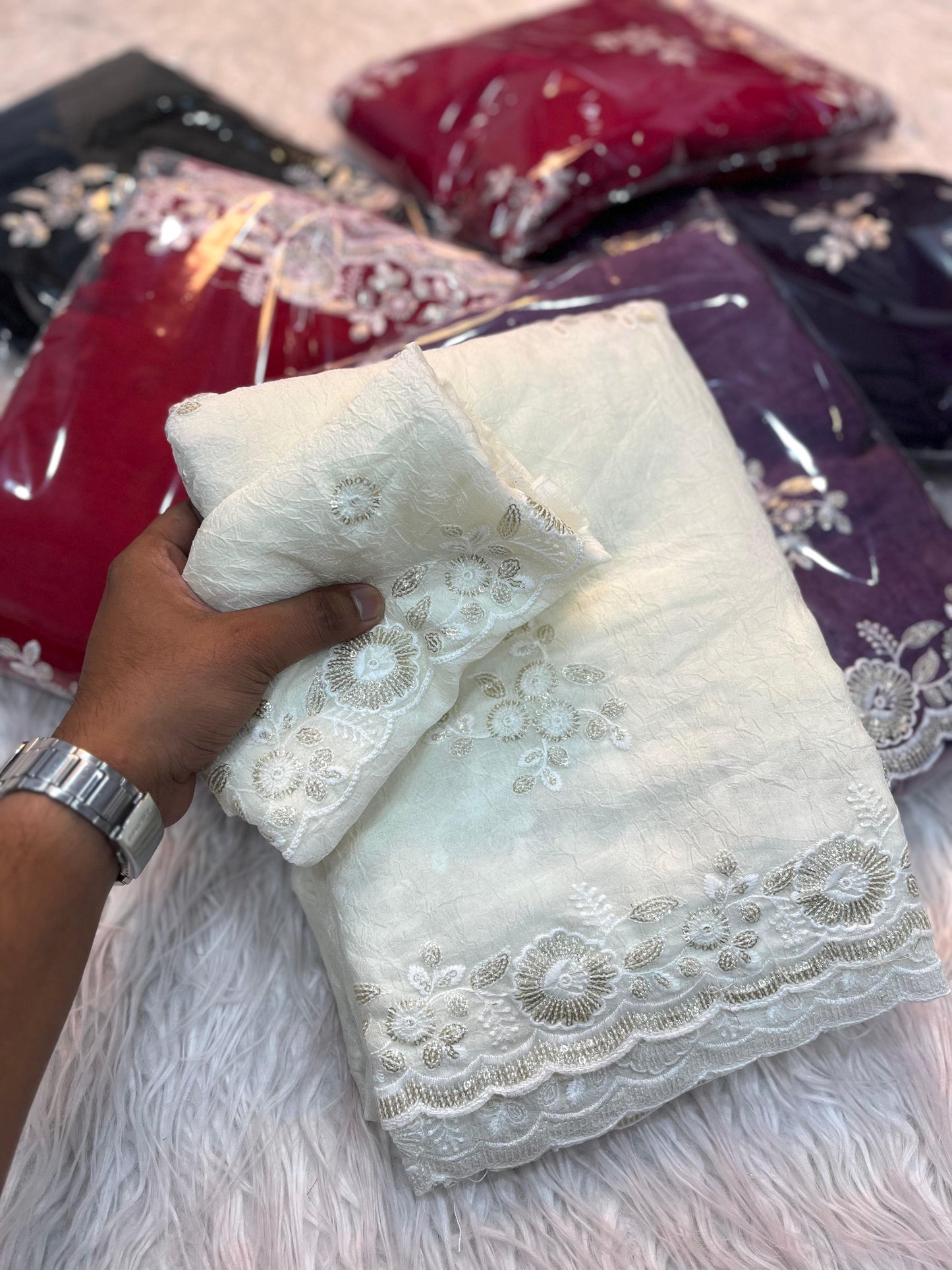 A luxurious off-white saree decorated with hand-embroidered floral motifs and elegant lacework along the edges. The ensemble includes a matching blouse piece, perfect for bridal wear or sophisticated festive occasions.