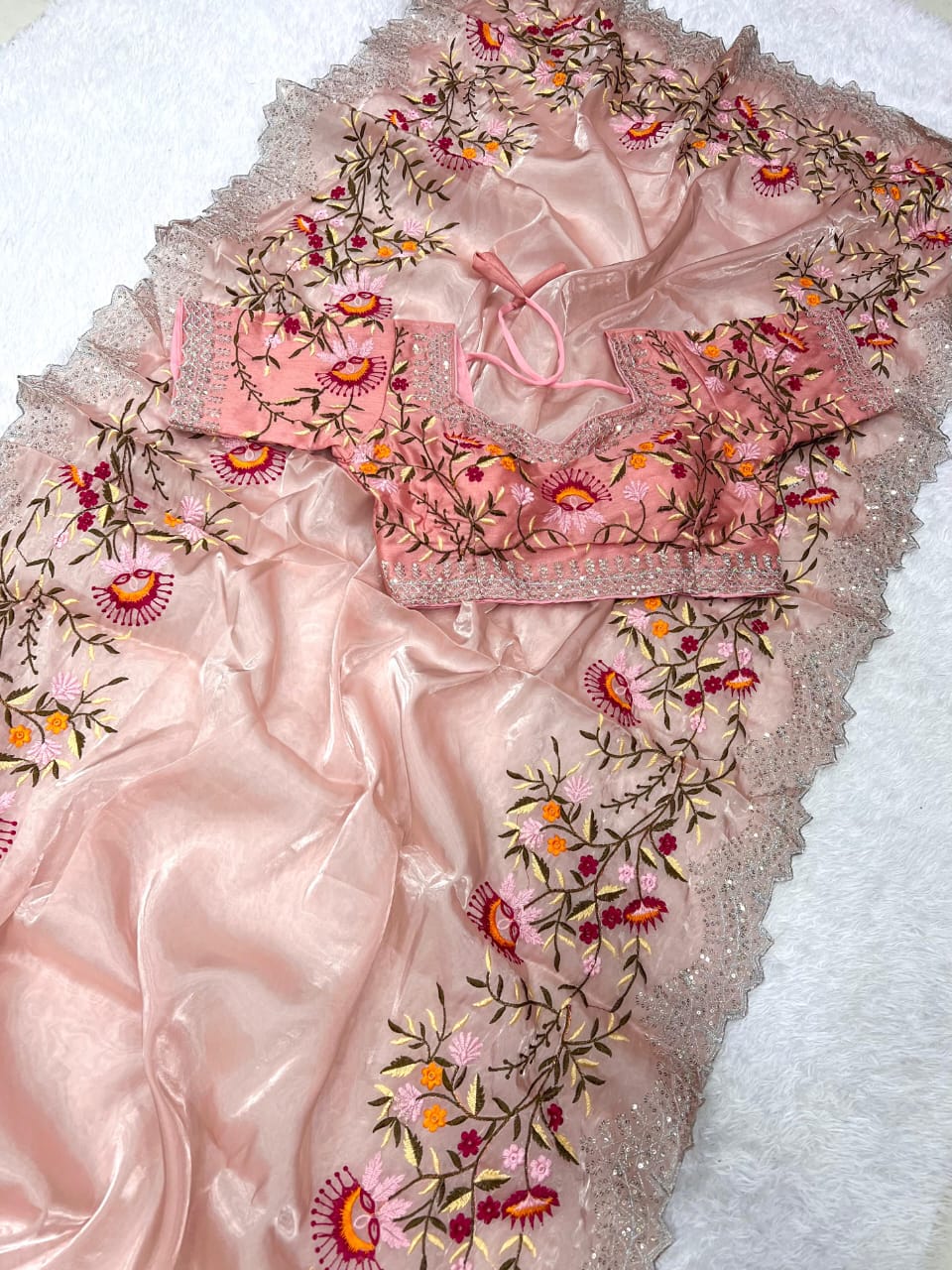 A pastel peach embroidered saree embellished with multicolor thread floral motifs and a detailed embroidered border. The ready blouse enhances the soft and elegant aesthetic, ideal for weddings, parties, and festive gatherings.