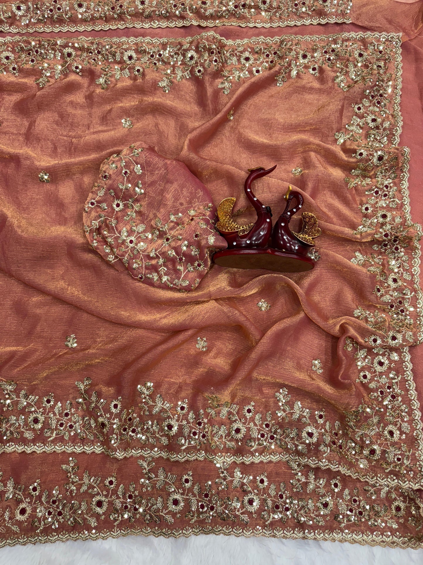 A luxurious peach-gold Fandy silk saree showcasing fine hand embroidery with golden threads and maroon accents. The scalloped border and matching blouse enhance its festive and bridal appeal.