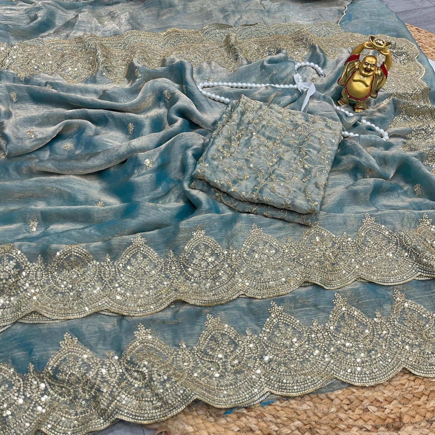 A stunning sea green saree featuring handcrafted golden zari embroidery and stone embellishments along the border. The matching blouse piece showcases detailed threadwork, giving the saree a grand bridal or festive appeal.