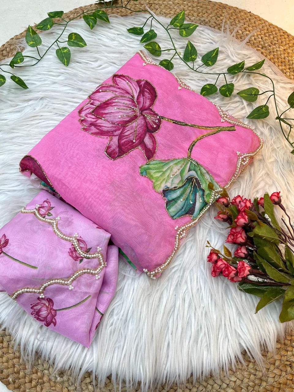 A soft organza saree in pastel pink featuring detailed lotus flower artwork and a handcrafted pearl scalloped border. The matching blouse enhances the saree’s festive and elegant appeal.