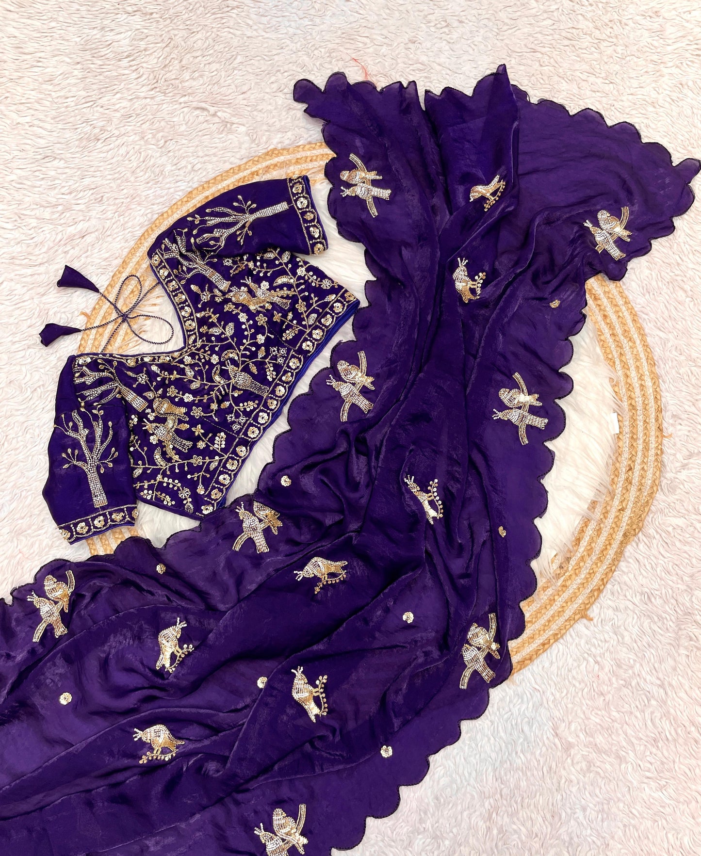 A velvet-toned purple space silk saree adorned with golden bird embroidery and a wavy scalloped border. The matching embroidered blouse enhances the saree’s festive and stylish appearance.