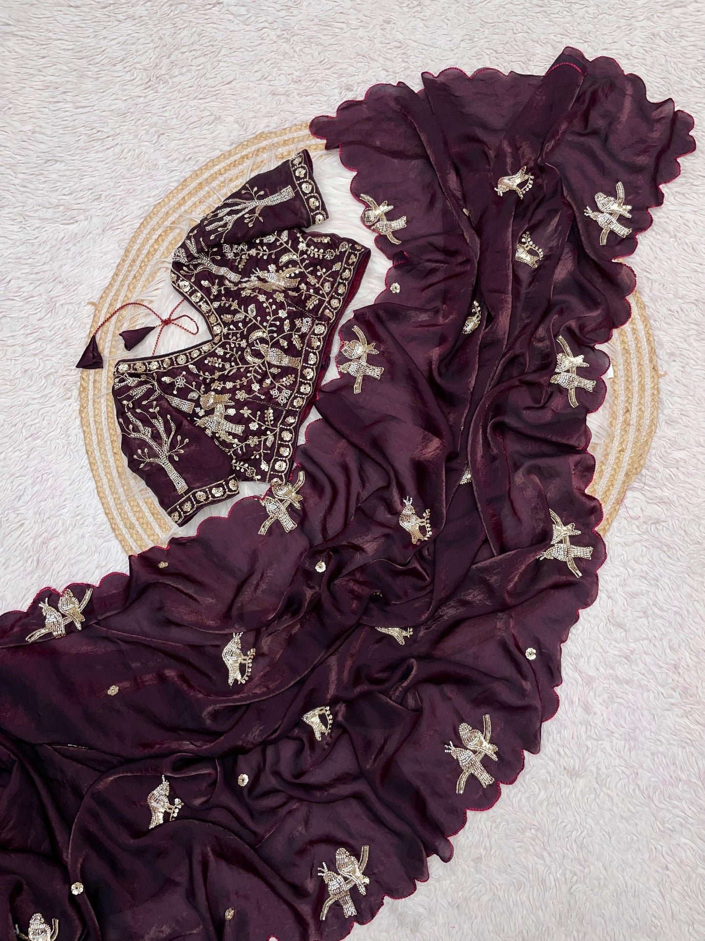A wine-maroon space silk saree embellished with golden bird motifs and delicate scalloped edges. The coordinating embroidered blouse enhances the saree’s regal and timeless charm, perfect for festive and ceremonial wear.