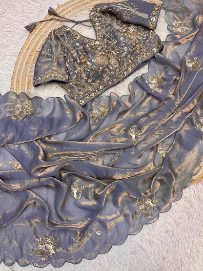 An ash grey silk saree adorned with subtle sequin bird embroidery and scalloped edging. The matching blouse showcases intricate threadwork and embellishments, blending minimal style with traditional elegance.