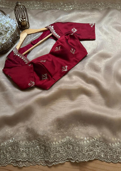 A beige gold saree with intricate zari embroidery along the border, paired with a rich wine-red embroidered blouse. The elegant color contrast and luxurious texture make it perfect for festive and wedding occasions.
