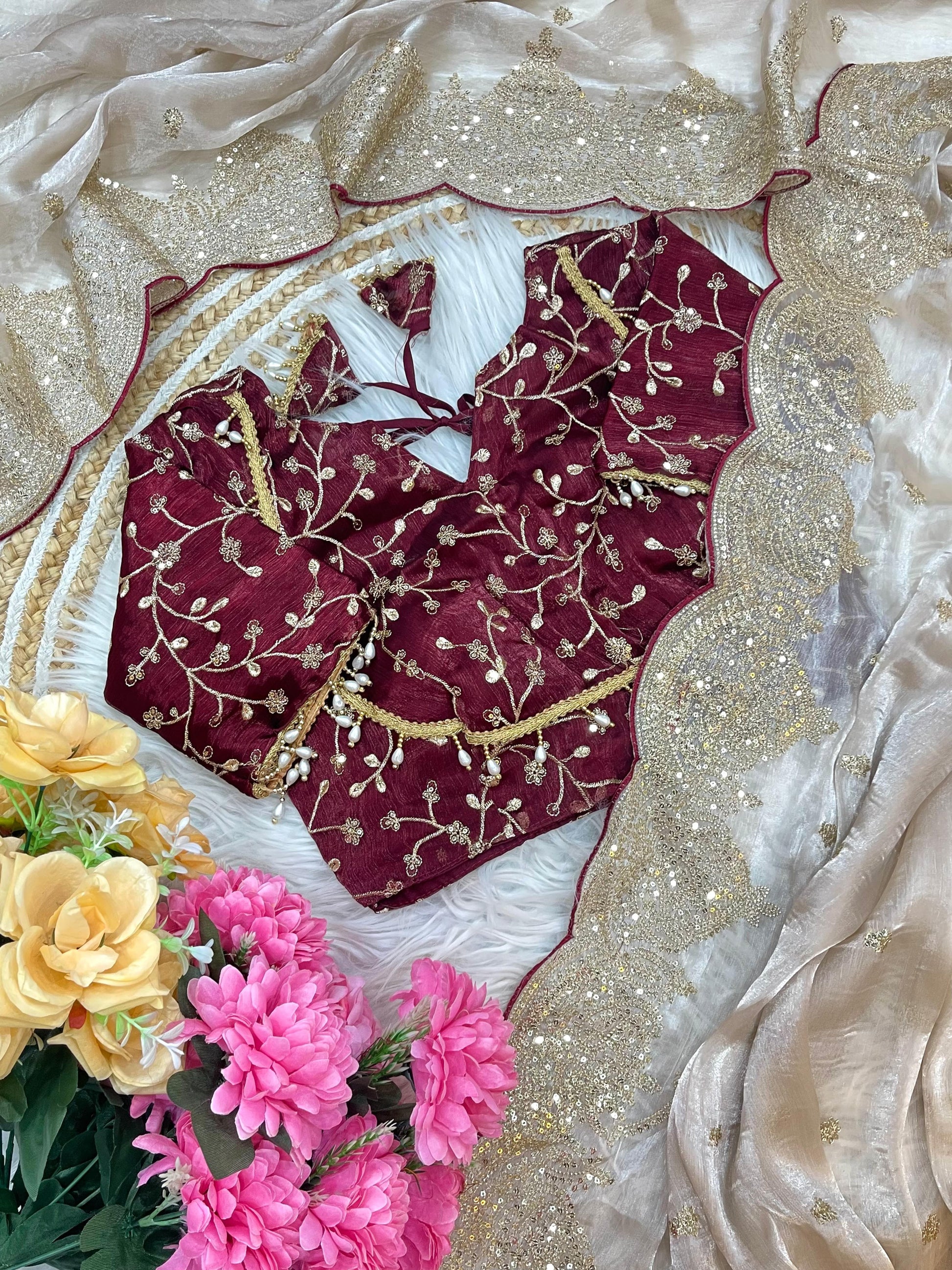 A beige net saree embellished with fine gold sequin embroidery and a scalloped border. The saree is styled with a rich maroon embroidered blouse, offering a perfect blend of sophistication and festive elegance.