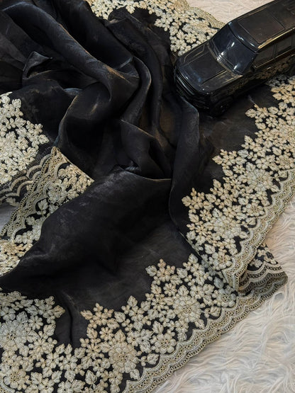 A classy black Fandy silk saree decorated with elegant white floral embroidery and a beautifully scalloped border. The matching blouse completes this stylish and graceful traditional ensemble.