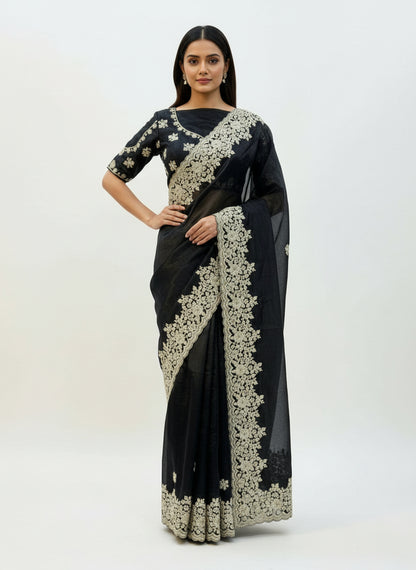A luxurious black Fandy silk saree featuring intricate white floral embroidery along the border and pallu. The saree is paired with a matching blouse embellished with coordinated floral motifs, creating a rich and elegant ethnic look.