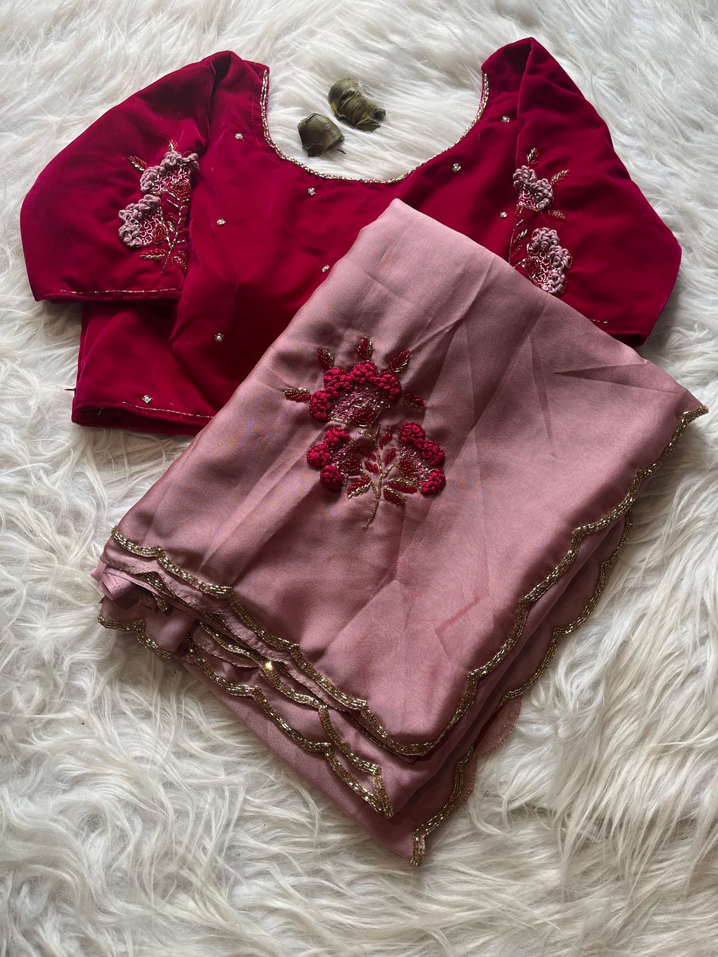 A luxurious Rangoli silk saree in blush pink, highlighted with elegant floral embroidery and a shimmery gold border. The ensemble is paired with a richly embroidered maroon velvet blouse, creating a sophisticated bridal or festive look.