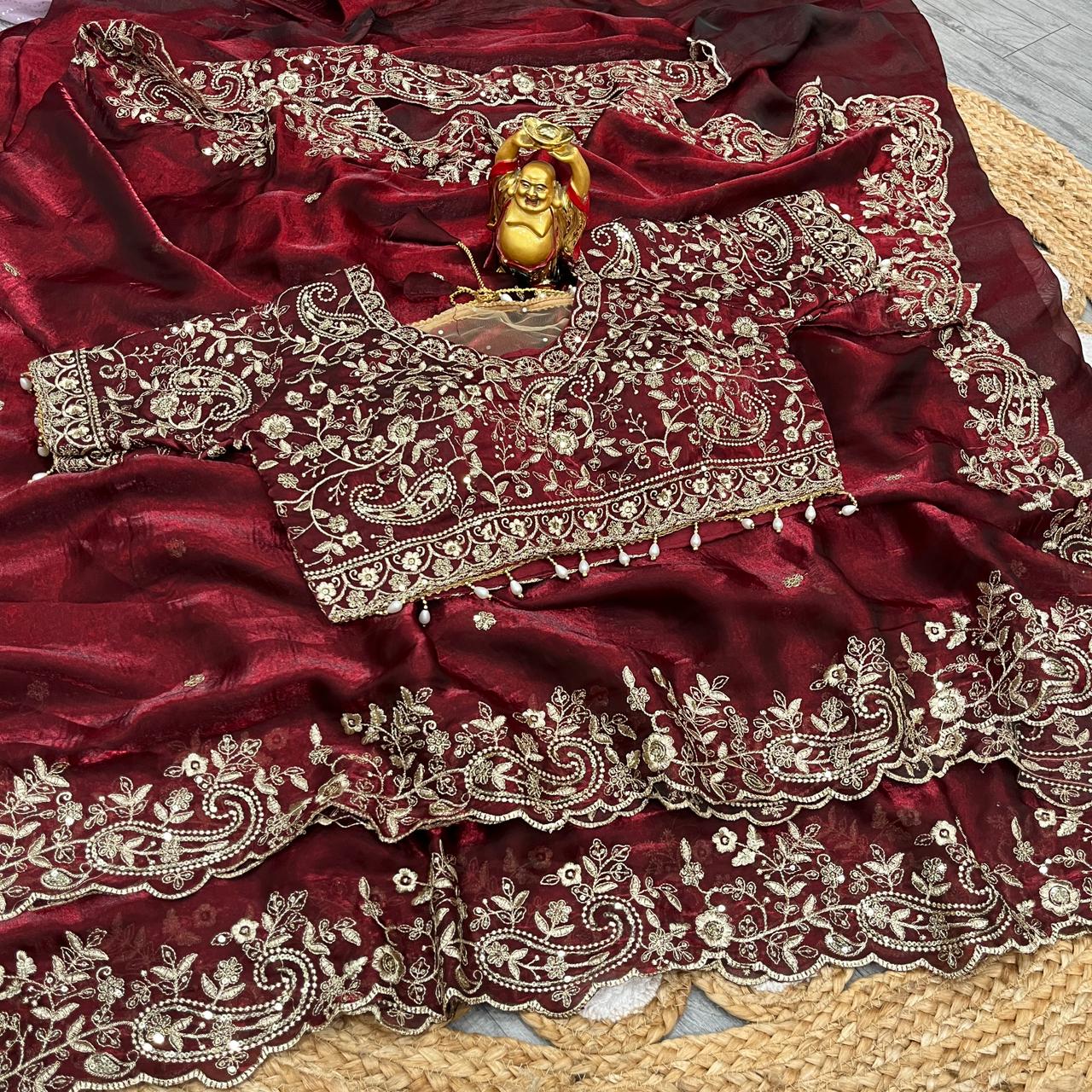 A bridal maroon soft space silk saree decorated with ornate golden floral embroidery and detailed border work. The designer blouse with intricate thread and sequin embroidery completes this luxurious wedding-ready ensemble.