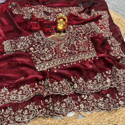 A bridal maroon soft space silk saree decorated with ornate golden floral embroidery and detailed border work. The designer blouse with intricate thread and sequin embroidery completes this luxurious wedding-ready ensemble.