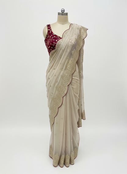 A mannequin draped in a champagne beige saree featuring a scalloped golden embroidered border and delicate floral sequin detailing. The saree is paired with a contrasting deep maroon velvet blouse adorned with intricate embroidery, creating a luxurious and graceful ethnic look.