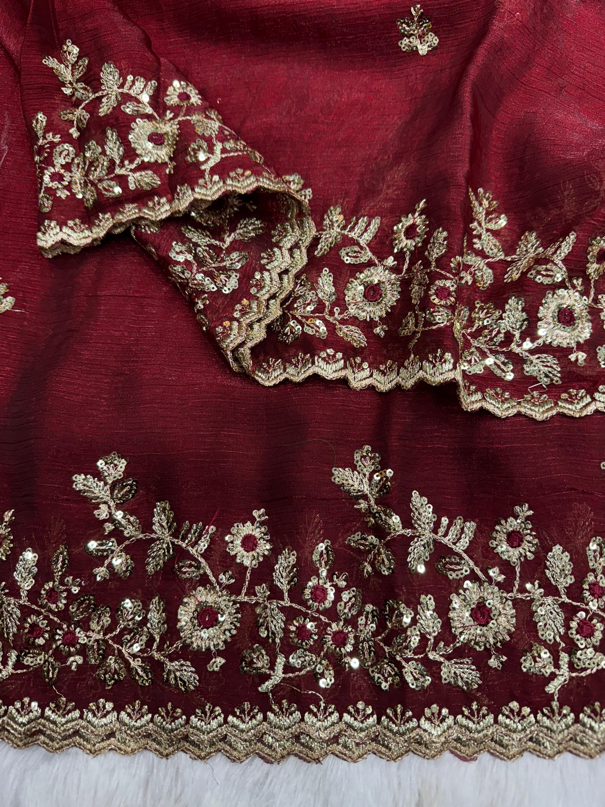 A dark maroon Fandy silk saree embellished with a detailed silver floral embroidered border and a matching designer blouse. The rich silk texture and ornate embroidery make it a perfect choice for weddings or festive events.