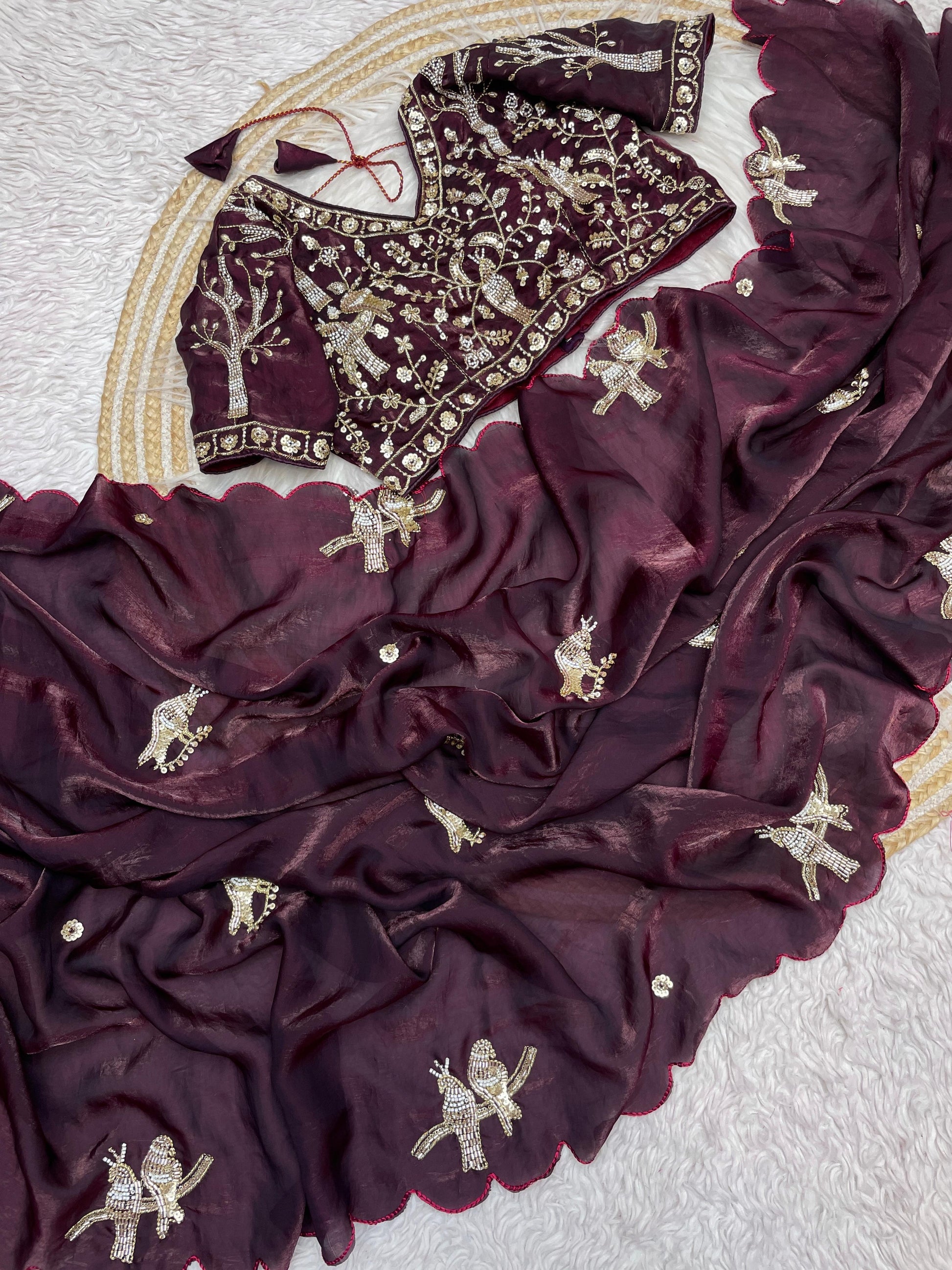 A deep maroon silk saree adorned with handcrafted golden bird embroidery and scalloped borders. The matching blouse with heavy sequin detailing adds a modern yet traditional elegance to the ensemble.