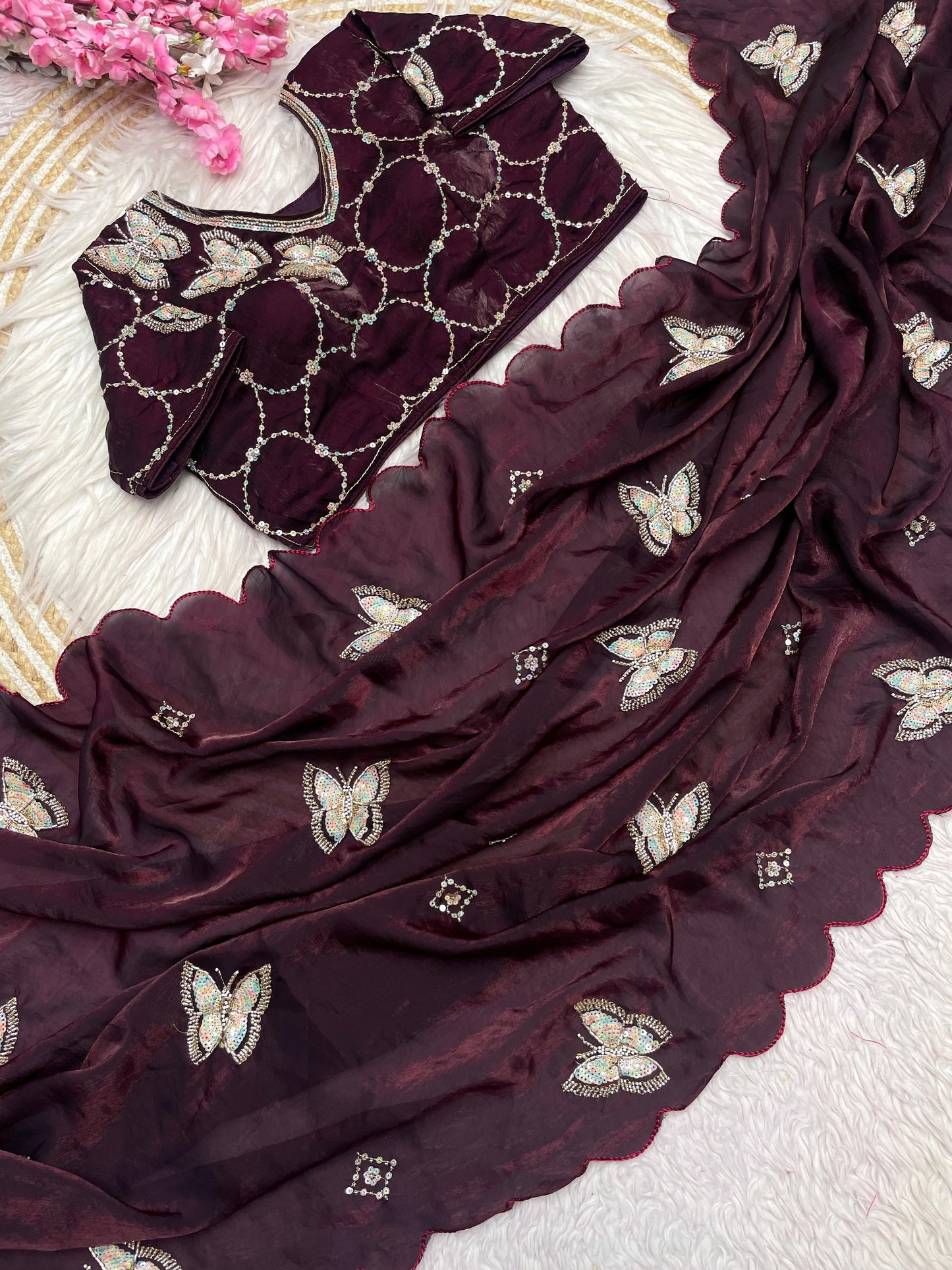 A deep maroon space silk saree decorated with delicate butterfly sequin embroidery and soft scalloped borders. The matching blouse features circular embroidered patterns, offering a trendy and sophisticated appeal.