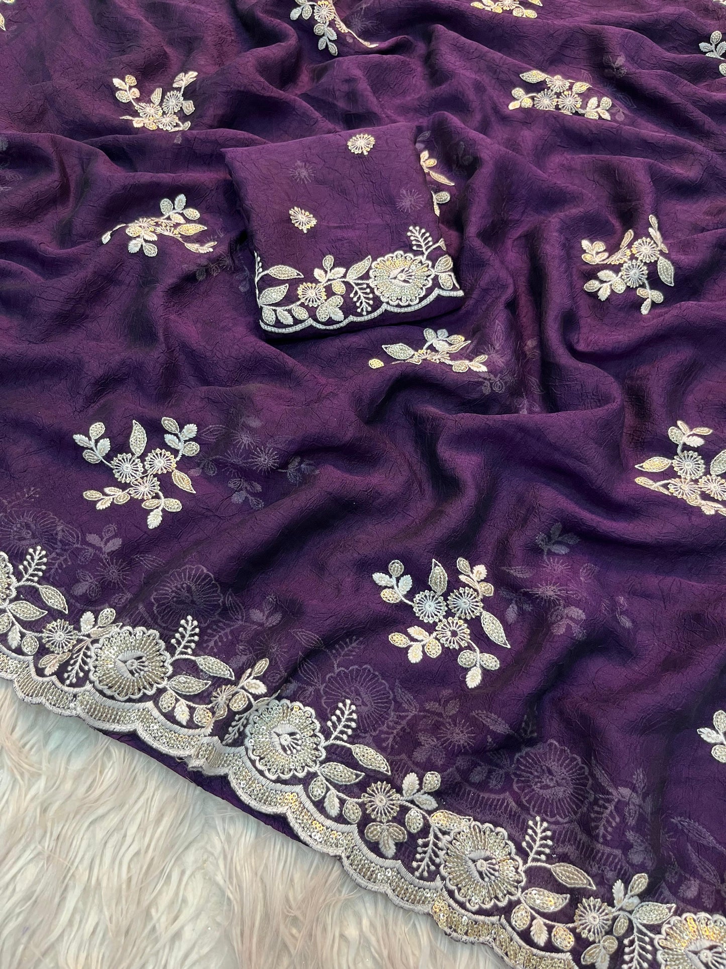 A mannequin dressed in a deep purple saree adorned with silver floral embroidery and a scalloped border. The saree is paired with a matching blouse featuring intricate embroidery on the neckline and sleeves, creating a timeless and graceful look.