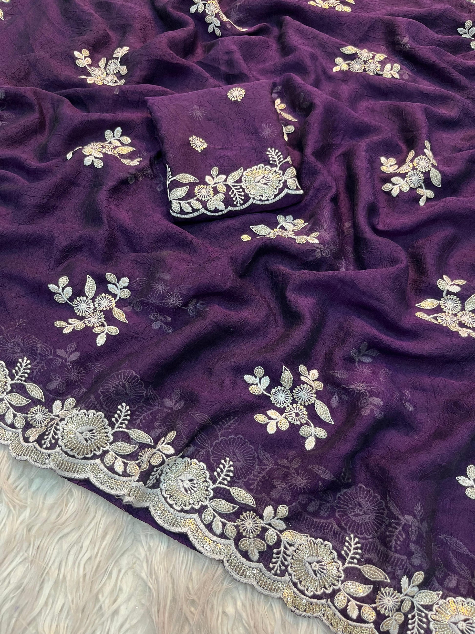 A mannequin dressed in a deep purple saree adorned with silver floral embroidery and a scalloped border. The saree is paired with a matching blouse featuring intricate embroidery on the neckline and sleeves, creating a timeless and graceful look.
