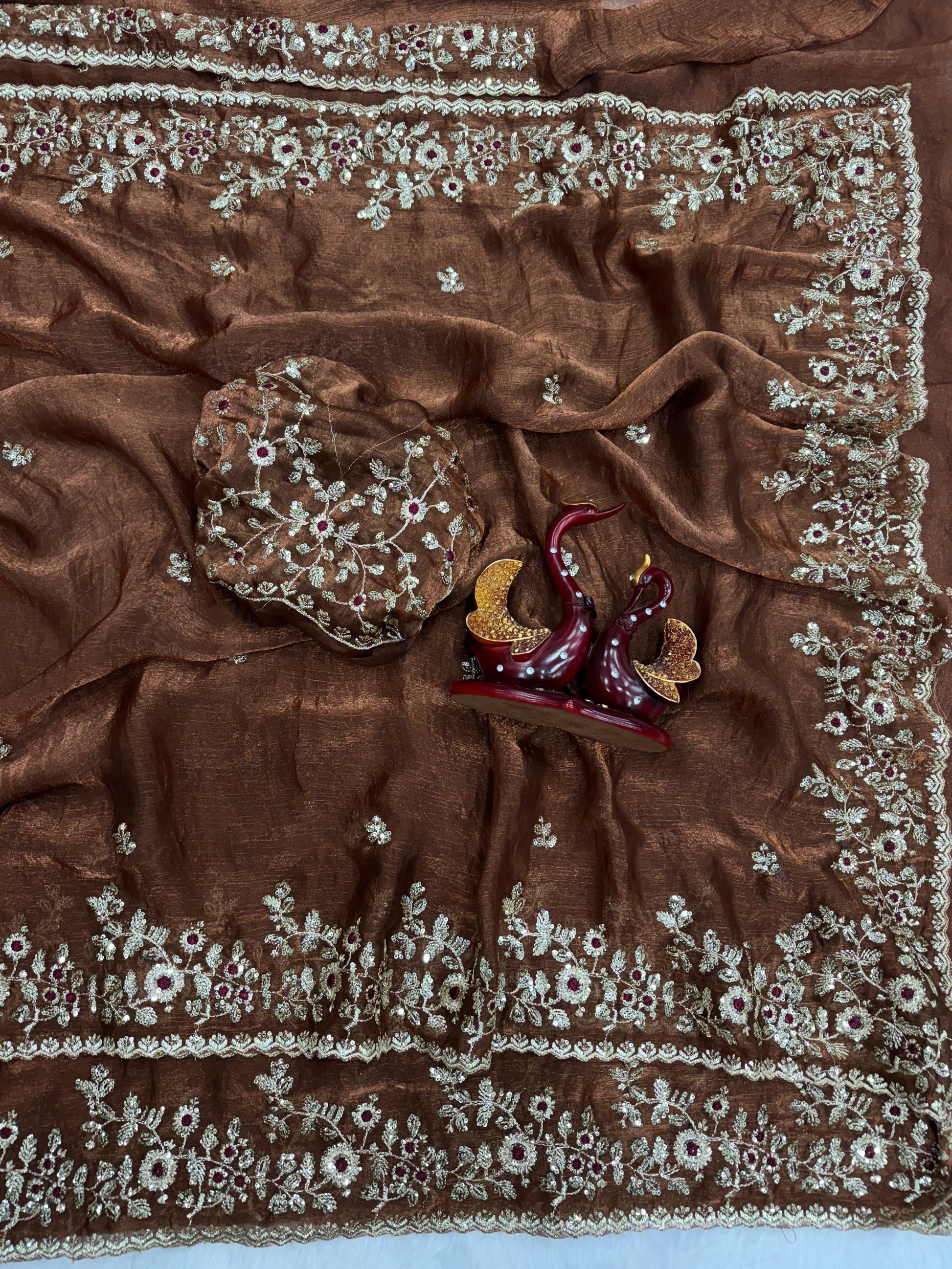 A luxurious designer chocolate Fandy silk saree featuring heavy floral embroidery with golden and maroon threadwork. The rich fabric and ornate border make it a perfect pick for festive and wedding occasions.