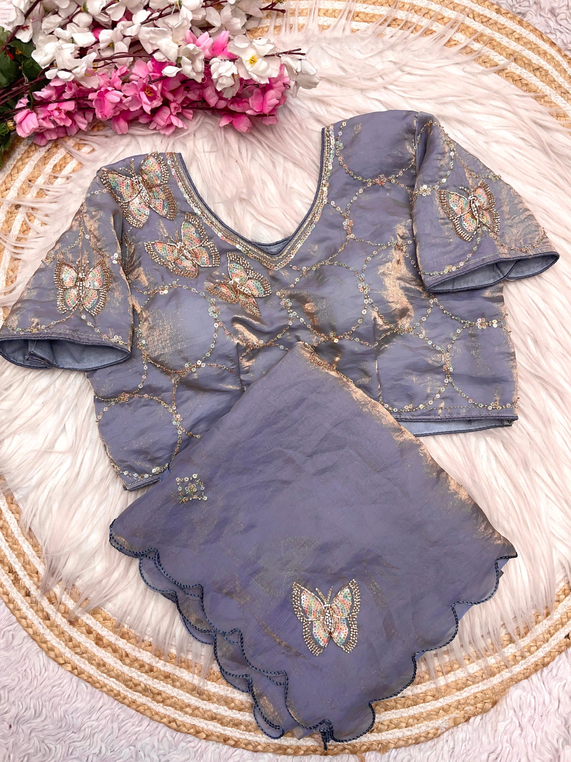 A luxurious grey space silk saree embellished with shimmering butterfly embroidery and scalloped detailing. The matching stitched blouse showcases circular sequin designs, making it a perfect choice for festive and party occasions.