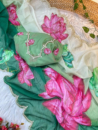A premium soft organza saree in dual tones of cream and green, beautifully adorned with watercolor-style lotus motifs in pink and green. The pearl scalloped edging and matching floral blouse add luxury and sophistication.