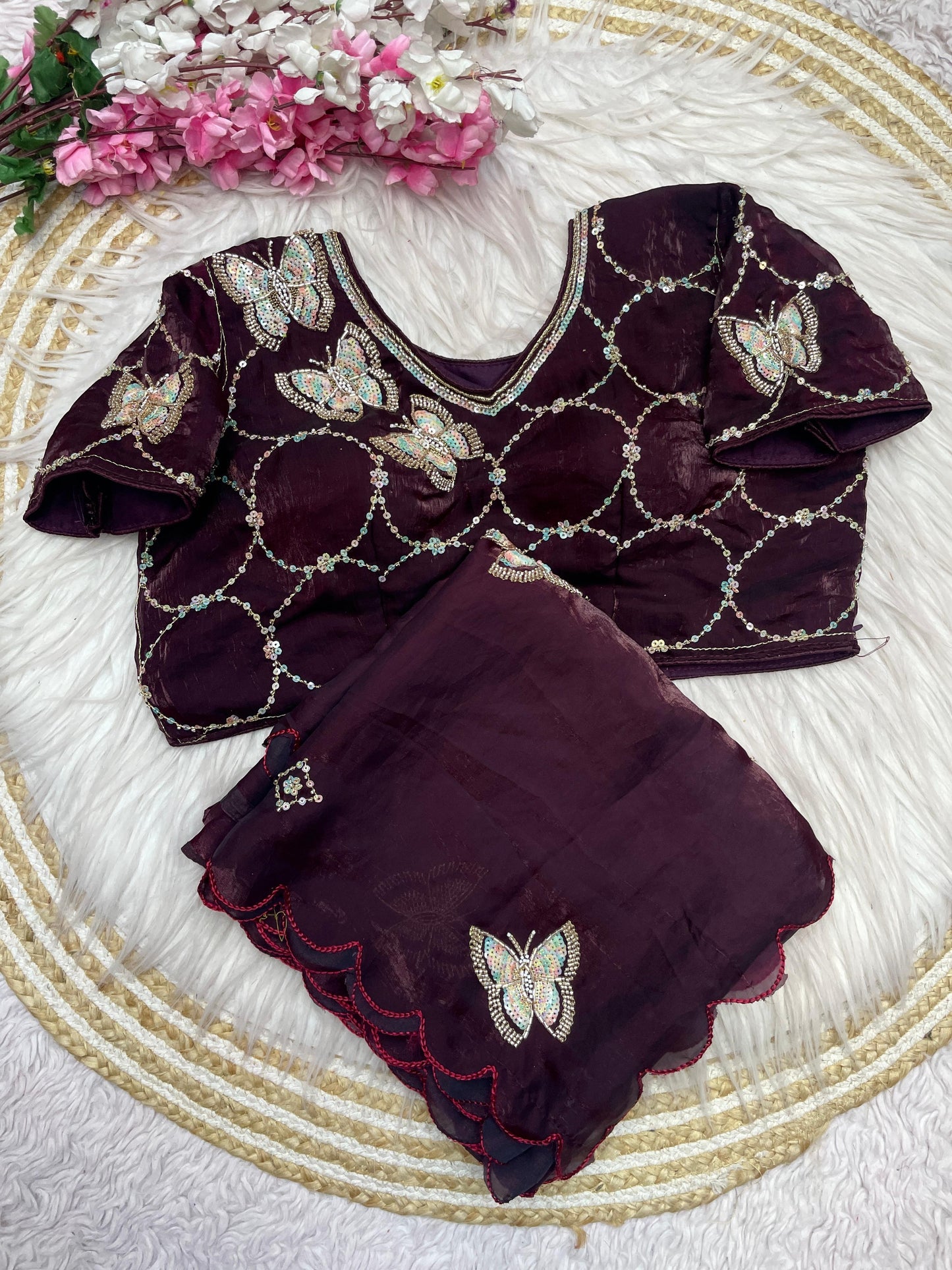 A luxurious maroon space silk saree beautifully detailed with shimmering butterfly embroidery and a scalloped edge. The outfit includes a stitched blouse with matching embroidery and geometric sequin work, ideal for weddings and parties.