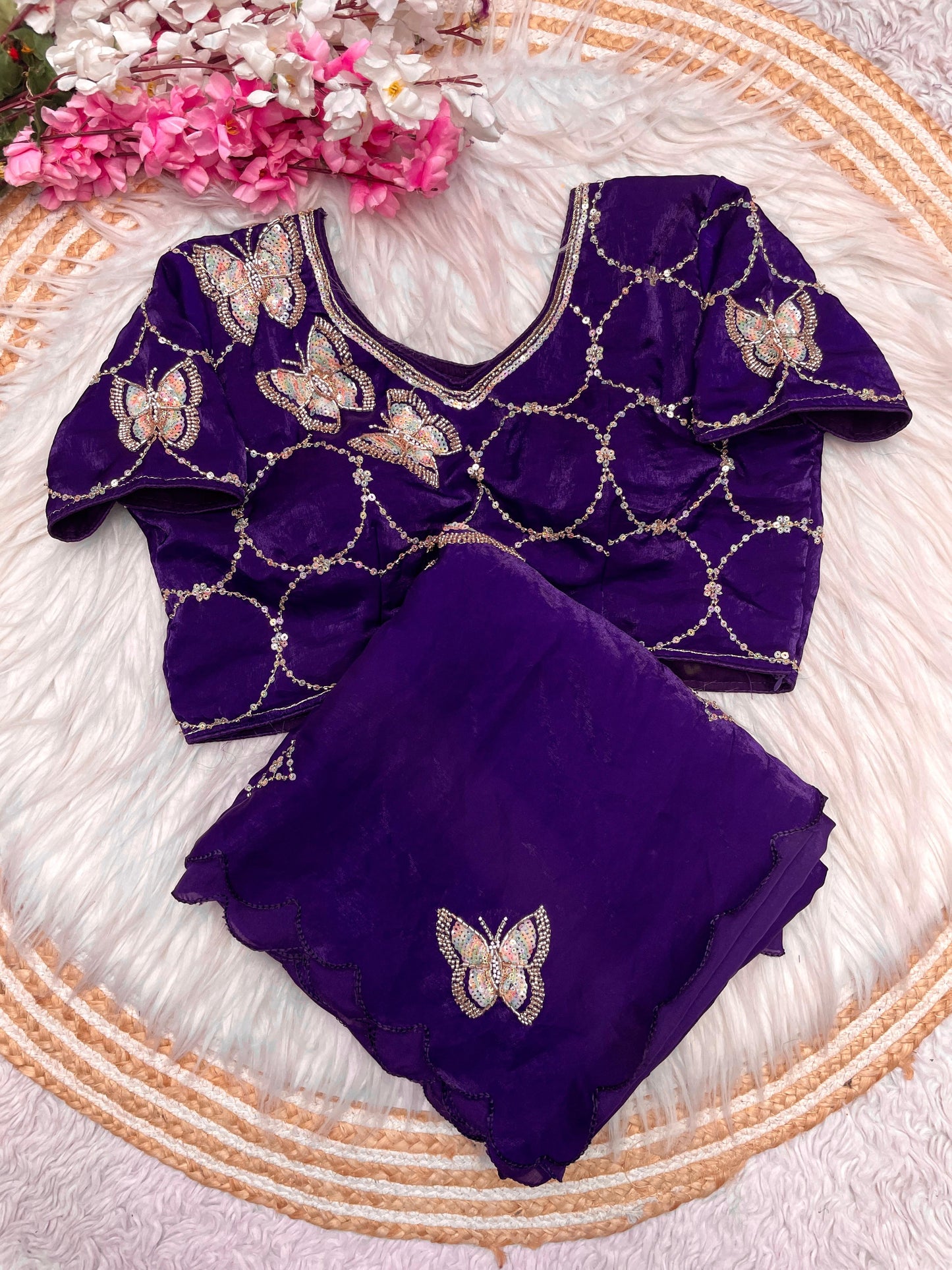 A designer purple space silk saree beautifully embellished with shimmering butterfly motifs and scalloped borders. The outfit includes a matching stitched blouse with embroidered circular patterns, blending traditional elegance with modern sophistication.