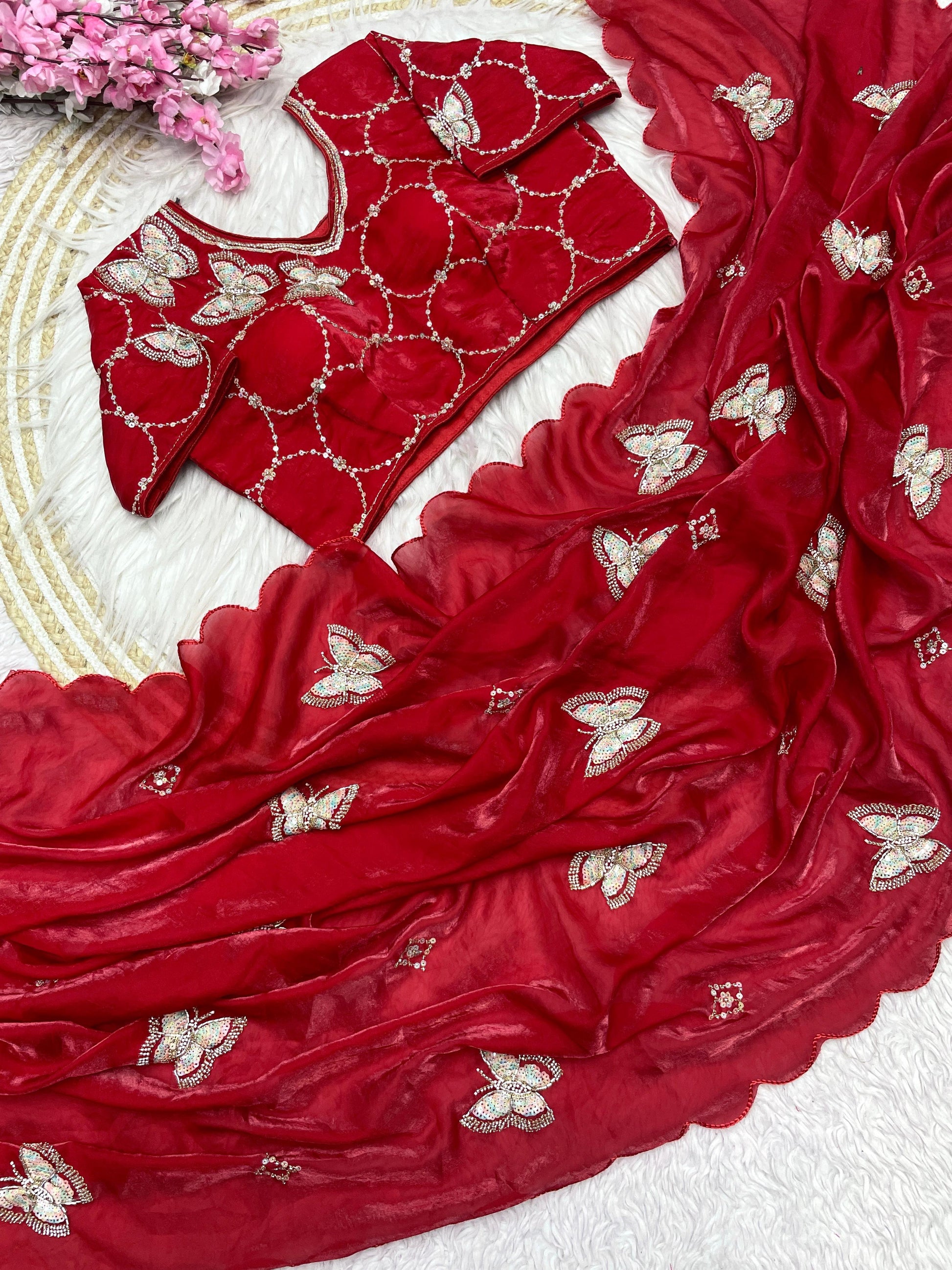 A luxurious red space silk saree decorated with elegant sequin-embroidered butterfly motifs and a scalloped border. The ensemble includes a matching stitched blouse with circular embroidered patterns, exuding bridal elegance and festive sophistication.