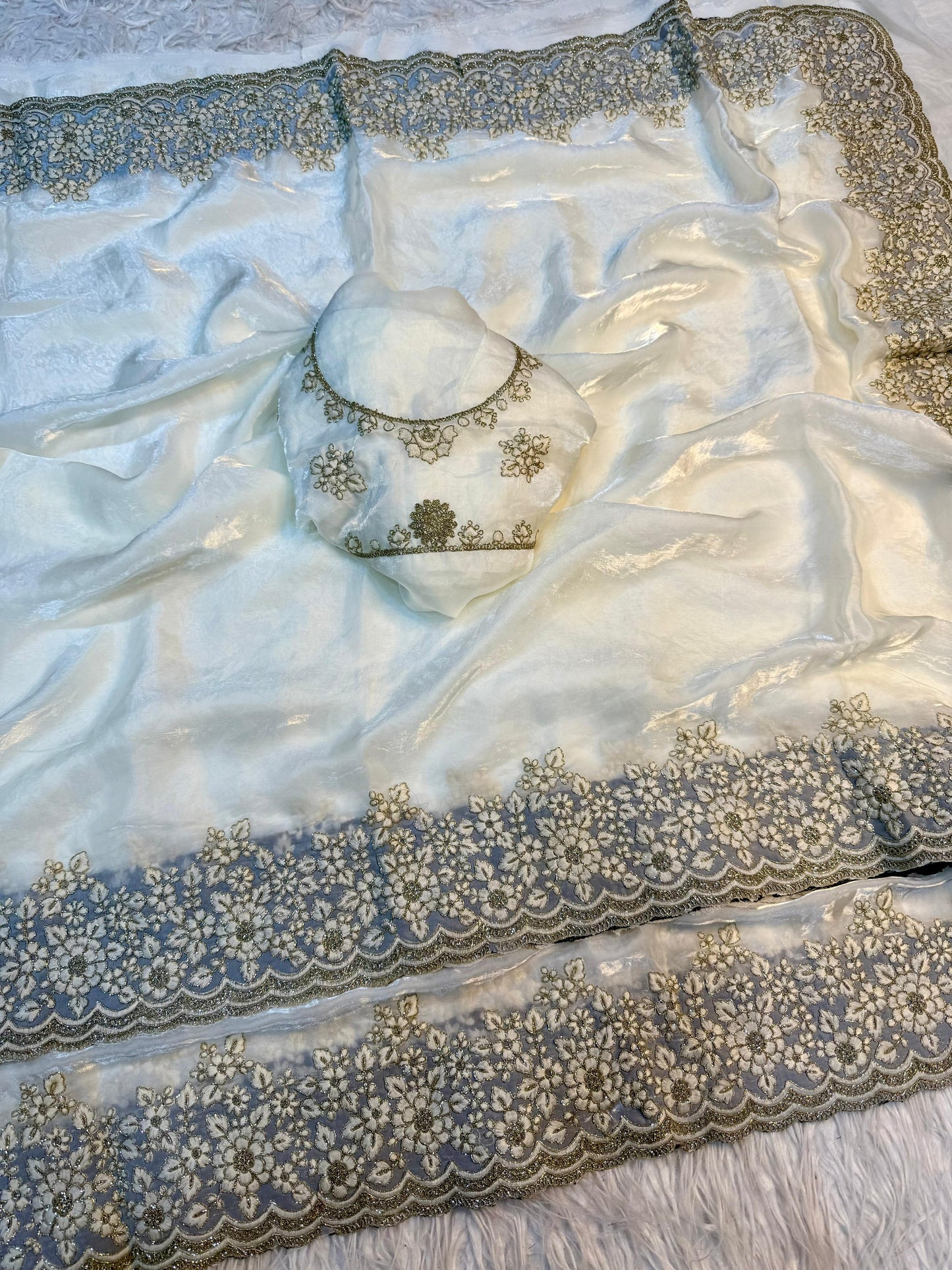 A premium white Fandy silk saree adorned with a handcrafted golden floral embroidered border. Paired with a matching embroidered blouse, this saree exudes luxury and sophistication, ideal for weddings and festive events.