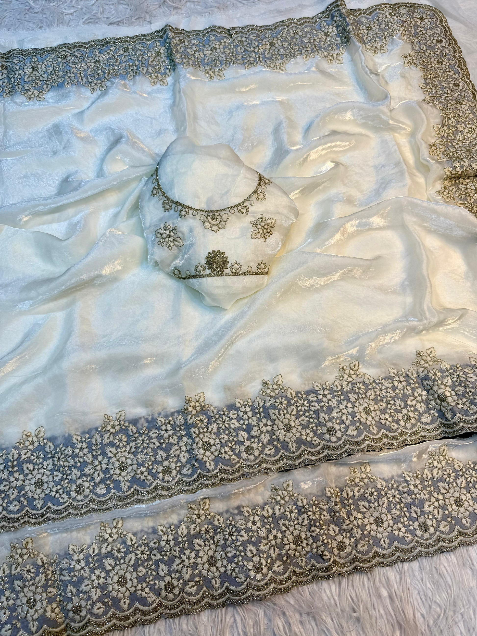 A premium white Fandy silk saree adorned with a handcrafted golden floral embroidered border. Paired with a matching embroidered blouse, this saree exudes luxury and sophistication, ideal for weddings and festive events.