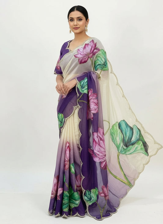 A luxurious dual-tone soft organza saree in cream and purple, featuring stunning hand-painted lotus flowers in pink and green shades. The saree is finished with a pearl-embellished scalloped border and comes with a matching blouse showcasing floral artwork, creating an elegant and artistic ethnic look.