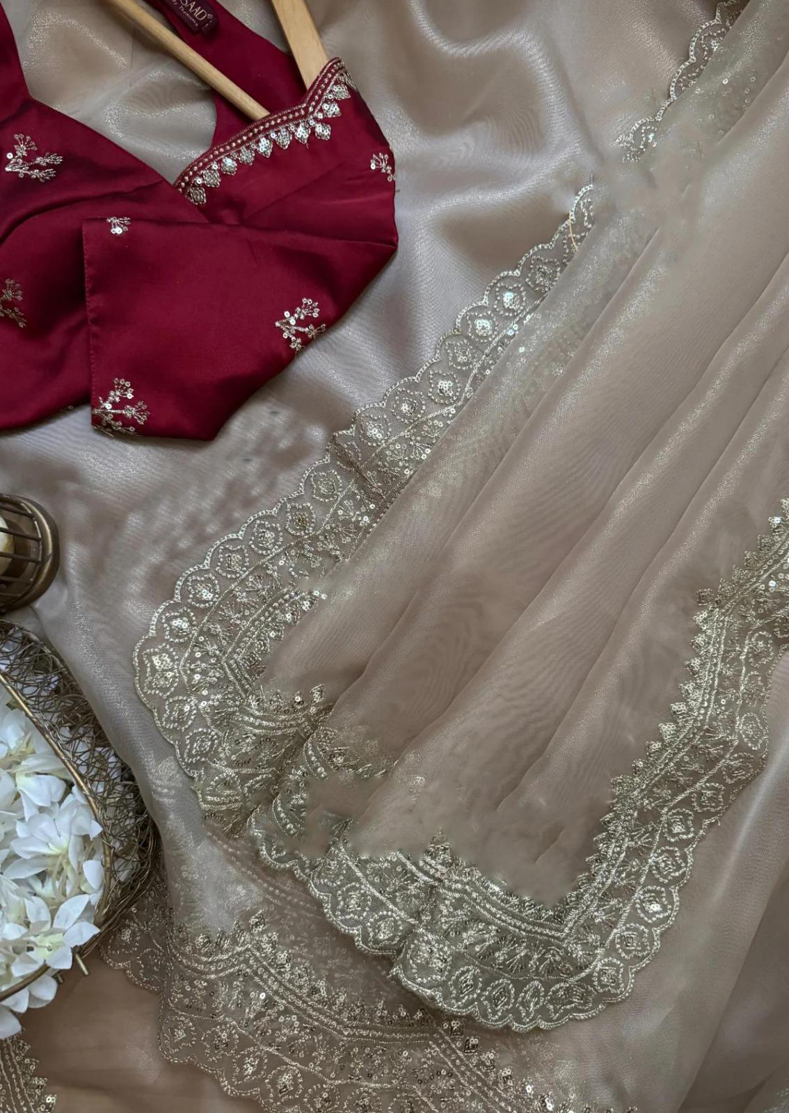 A stunning golden beige saree draped gracefully on a mannequin, detailed with delicate embroidery along the edges. It is paired with a handcrafted maroon blouse, adding a touch of royal elegance to the ensemble.