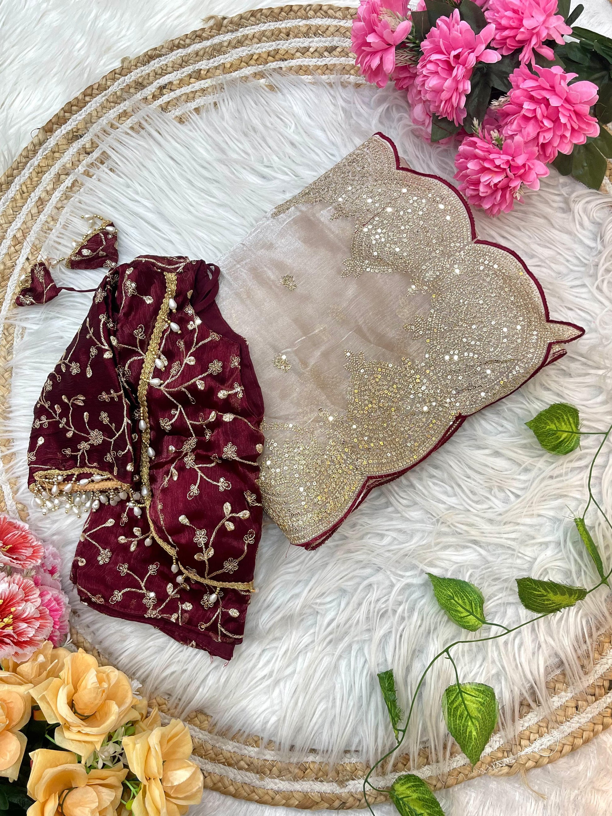 A stunning golden beige saree adorned with a scalloped heavy embroidered border and scattered floral motifs. Paired with a maroon velvet embroidered blouse, this ensemble exudes regal charm, ideal for weddings and festive occasions.