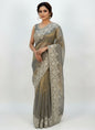 A sophisticated grey Fandy silk saree embellished with intricate white floral embroidery along the border. The saree includes a matching blouse featuring coordinated embroidery on the neckline and sleeves, creating an elegant and festive ethnic ensemble.