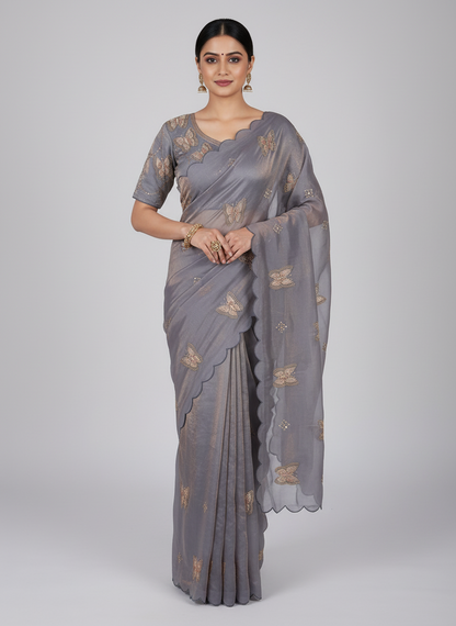 A stylish grey space silk saree adorned with intricate embroidered butterfly motifs and scalloped edges. The saree is paired with a matching stitched blouse featuring geometric sequin embroidery, creating a graceful and contemporary ethnic look.