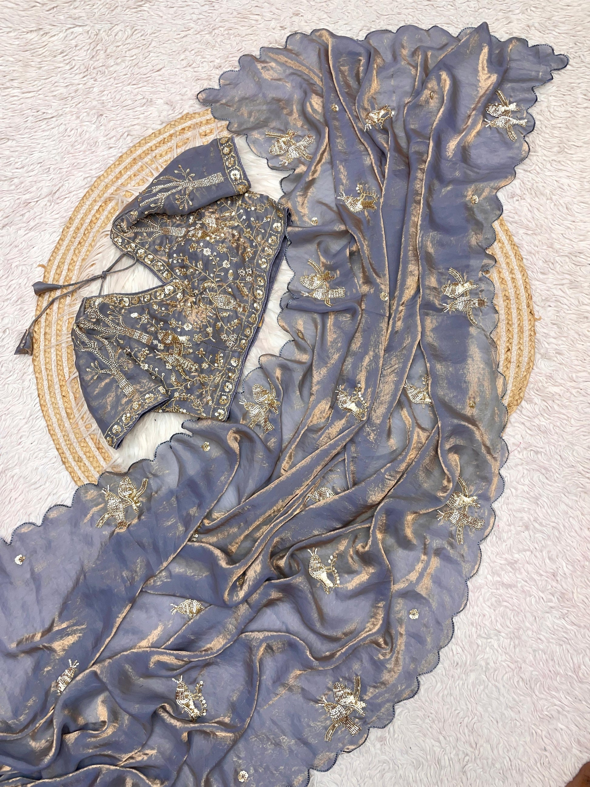 A designer grey space silk saree featuring golden embroidered bird motifs and shimmering scalloped borders. The matching stitched blouse, richly decorated with sequin and bead detailing, adds a luxurious touch to this elegant ensemble.