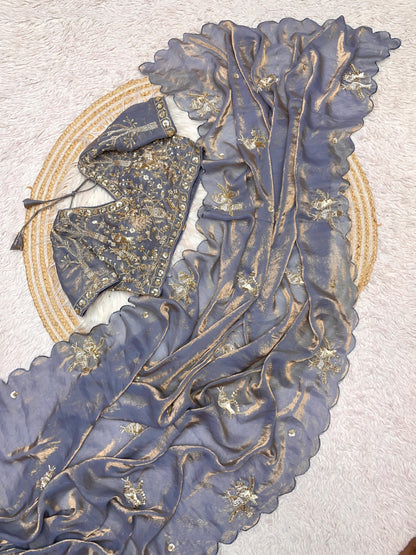 A designer grey space silk saree featuring golden embroidered bird motifs and shimmering scalloped borders. The matching stitched blouse, richly decorated with sequin and bead detailing, adds a luxurious touch to this elegant ensemble.