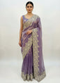 A soft lavender Fandy silk saree beautifully embellished with intricate white floral embroidery along the border. The saree includes a matching blouse featuring coordinated white thread and bead embroidery, creating a graceful and festive ethnic look.