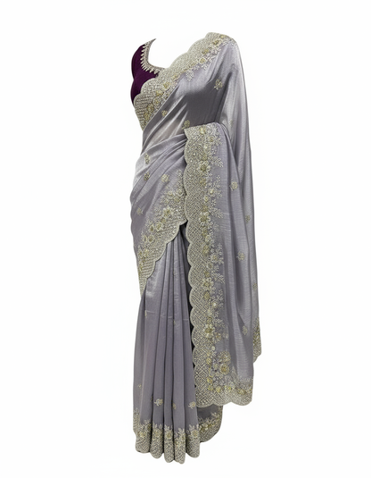 A soft lavender organza saree adorned with intricate silver and gold sequin embroidery along a scalloped border. The saree has a delicate shimmer and is paired with a contrasting deep magenta blouse piece, arranged elegantly in a woven basket on a white fur background.
