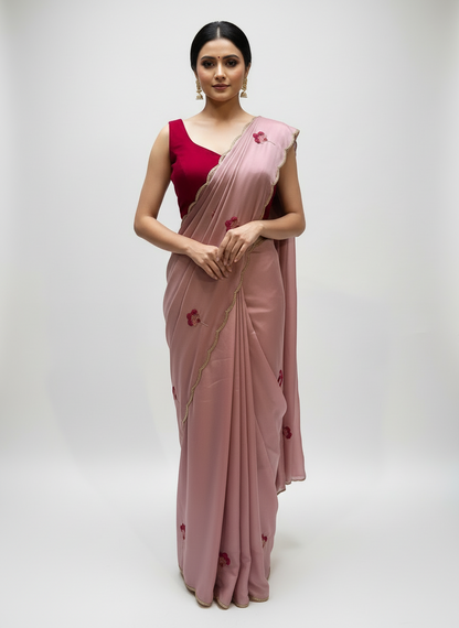 A beautiful Rangoli silk saree in soft mauve pink, paired with a deep maroon velvet blouse. Both saree and blouse feature delicate floral embroidery with golden bead accents, laid gracefully on a white fur background, showcasing rich texture and elegance.