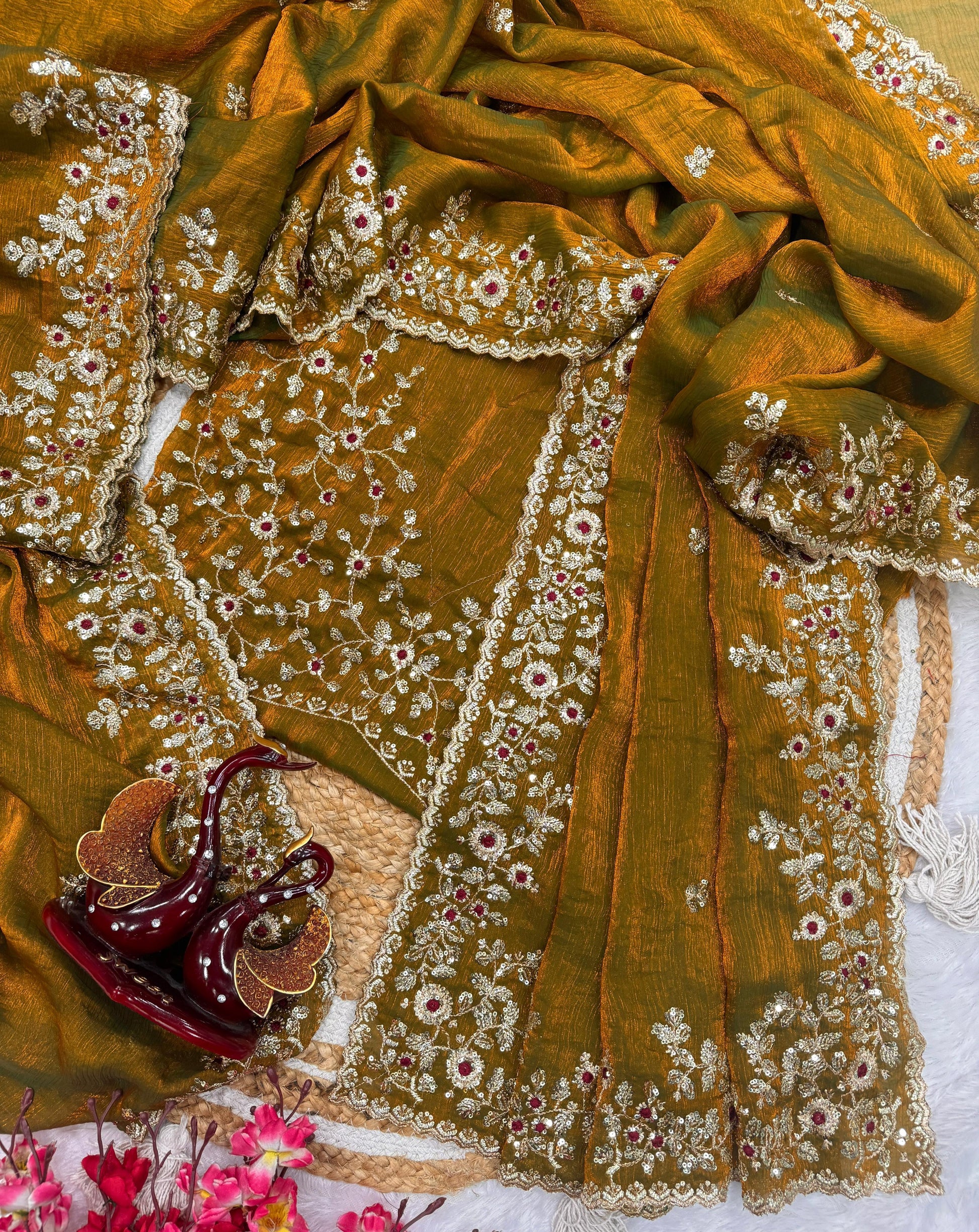 A mustard gold Fandy silk saree adorned with delicate zari embroidery, sequin highlights, and maroon floral accents. The heavy embroidered border adds grandeur, making it perfect for festive and wedding occasions.