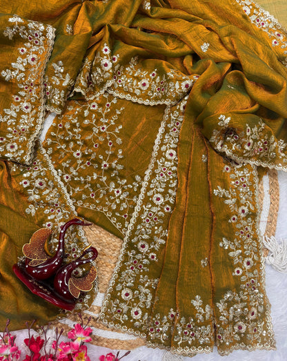 A mustard gold Fandy silk saree adorned with delicate zari embroidery, sequin highlights, and maroon floral accents. The heavy embroidered border adds grandeur, making it perfect for festive and wedding occasions.
