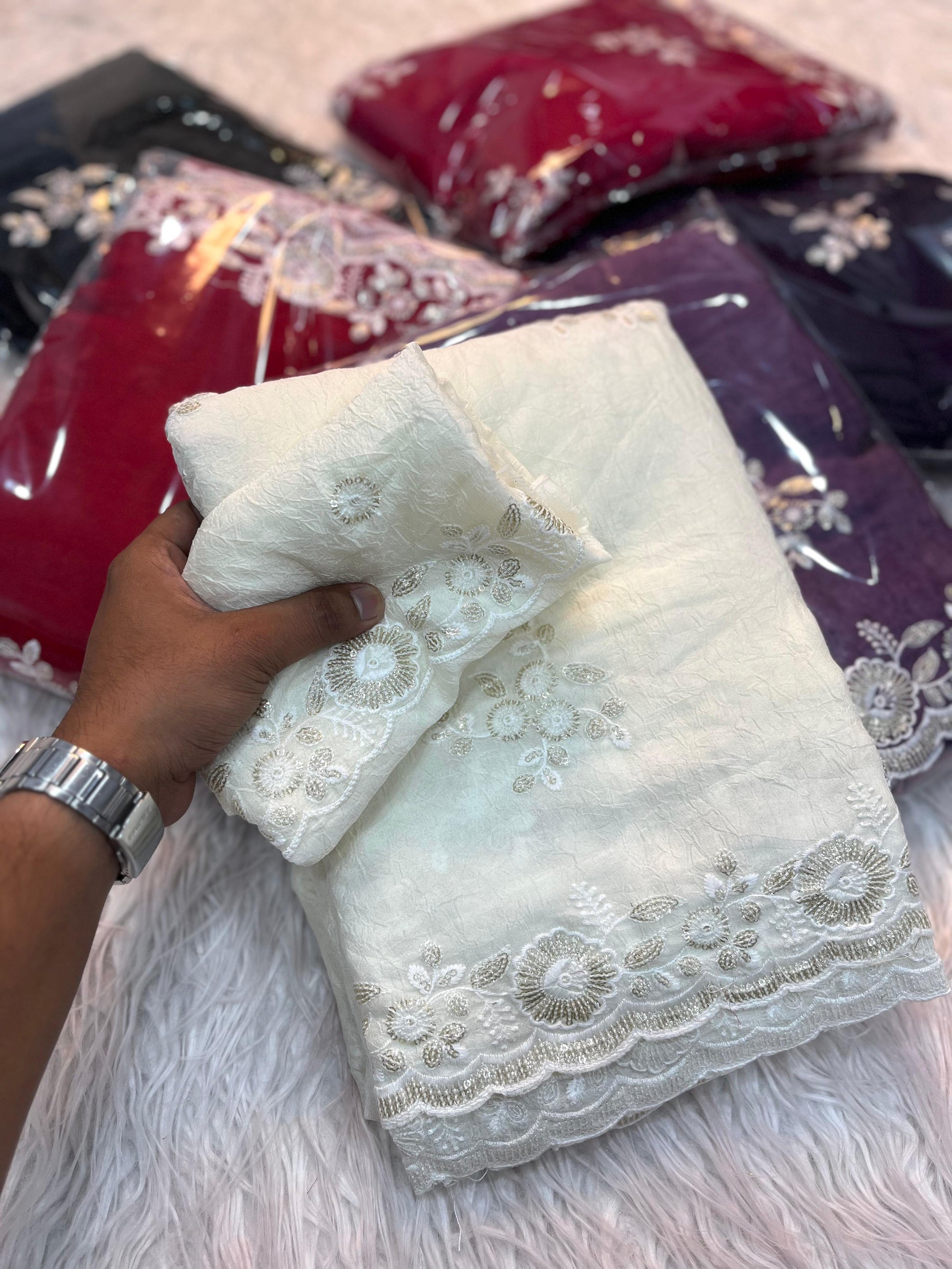 A luxurious off-white saree decorated with hand-embroidered floral motifs and elegant lacework along the edges. The ensemble includes a matching blouse piece, perfect for bridal wear or sophisticated festive occasions.