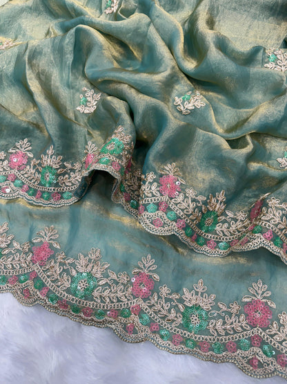 A woman dressed in a pastel blue space silk saree adorned with sequin floral embroidery. The saree is paired with a matching blouse and pearl choker, creating a sophisticated and romantic look perfect for festive occasions.