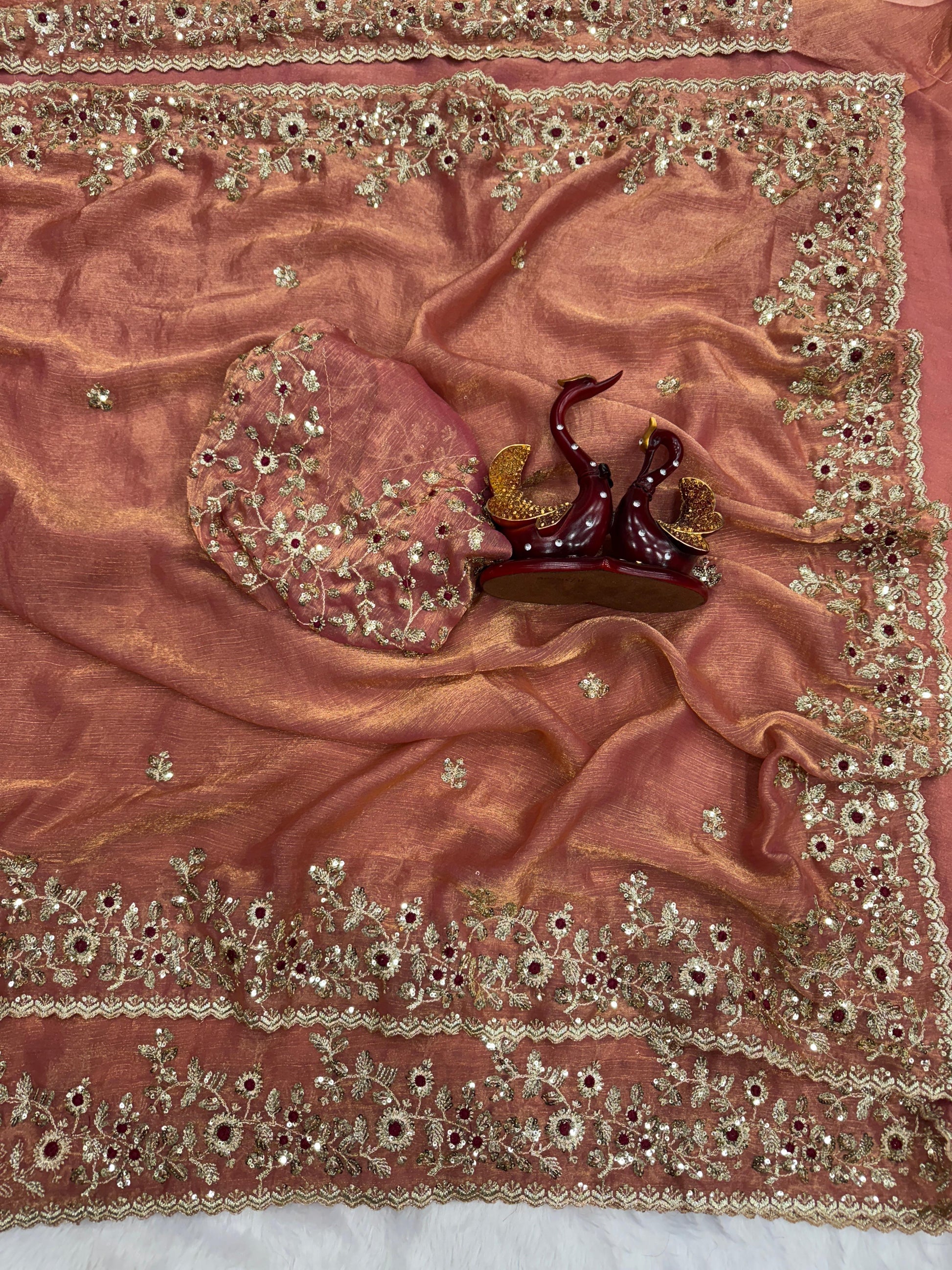 A luxurious peach-gold Fandy silk saree showcasing fine hand embroidery with golden threads and maroon accents. The scalloped border and matching blouse enhance its festive and bridal appeal.