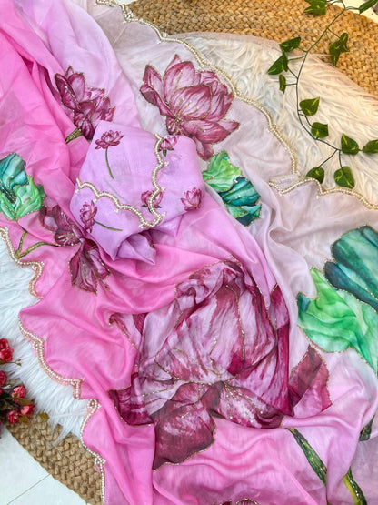 A modern pink organza saree showcasing large artistic floral prints and a pearl-embellished scalloped edge. Paired with a matching blouse decorated with floral accents, it offers a fresh and stylish ethnic look.