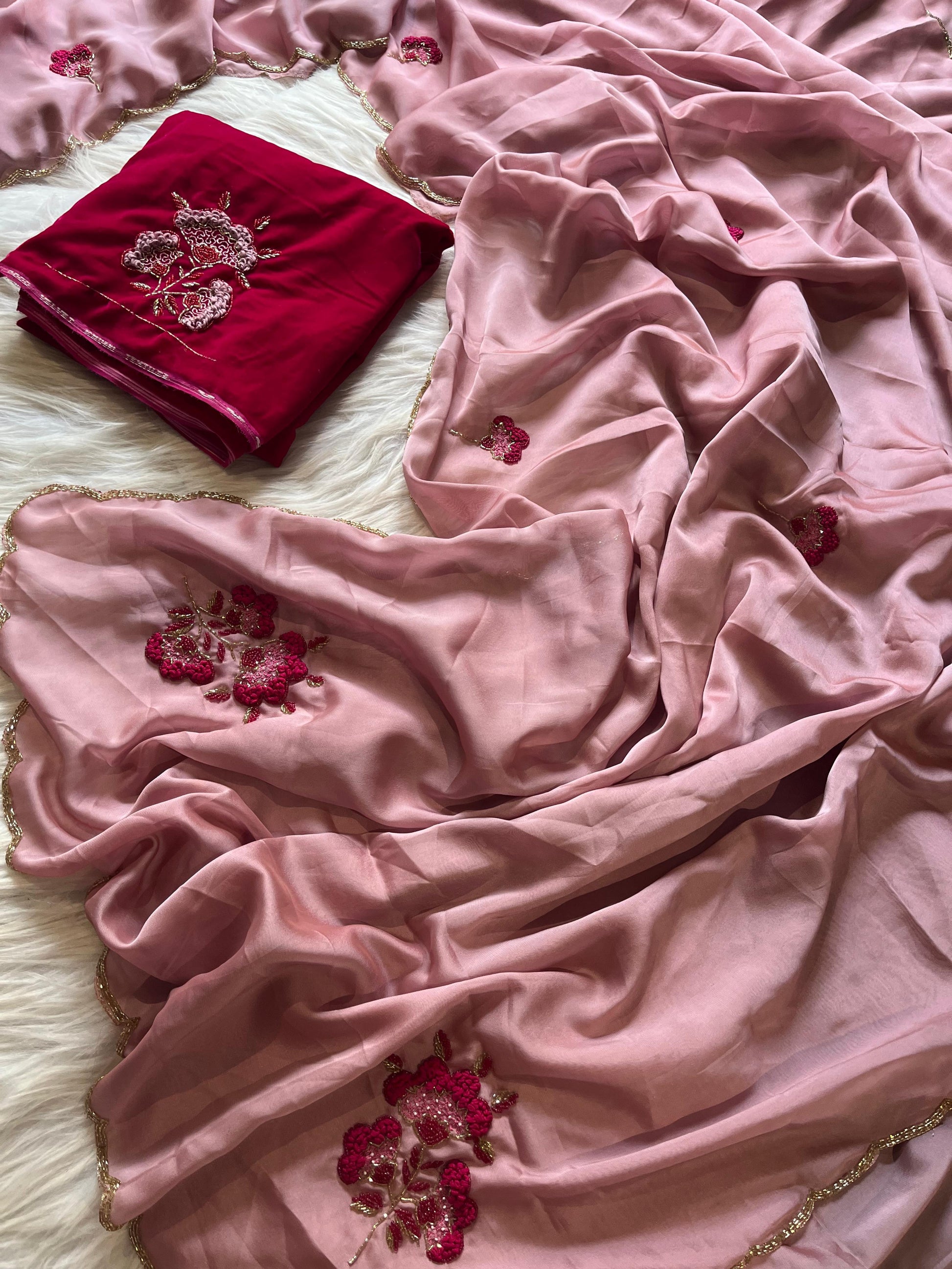 A trendy pink Rangoli silk saree styled with a wine-colored velvet blouse embellished with floral embroidery. The combination of soft silk and rich velvet creates a modern yet traditional festive outfit.